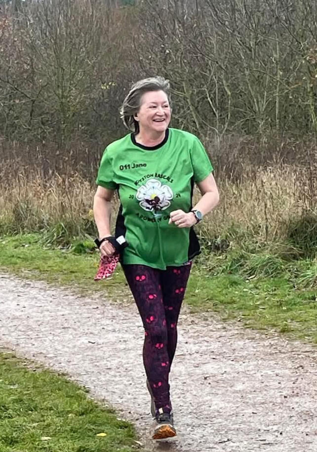 Action shot of woman in club shirt running on muddy path.
